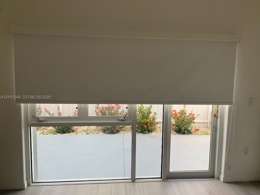 Large window and sliding glass door combination with white framing, retractable roller shade, and light-toned wood-finish flooring
