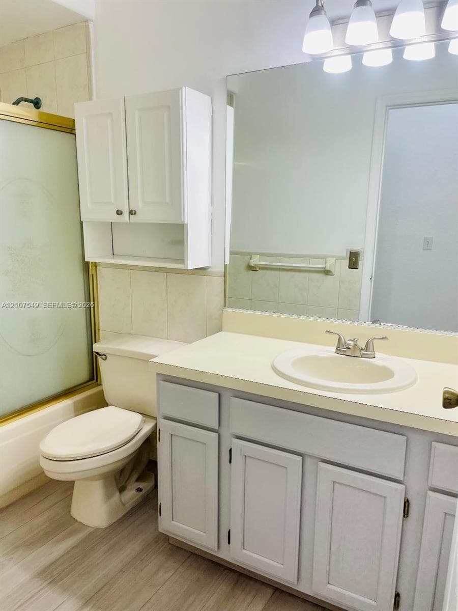 Bathroom featuring a vanity with an integrated sink, wood-finish flooring, a wall-mounted storage cabinet, a large vanity mirror, and a tub-shower combination with a sliding glass door