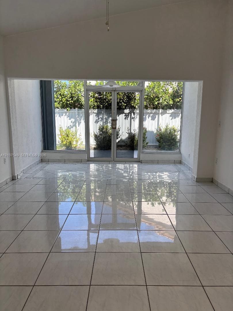 Open-concept space featuring polished ceramic tile flooring, vaulted ceilings, and expansive glass double doors with flanking floor-to-ceiling windows