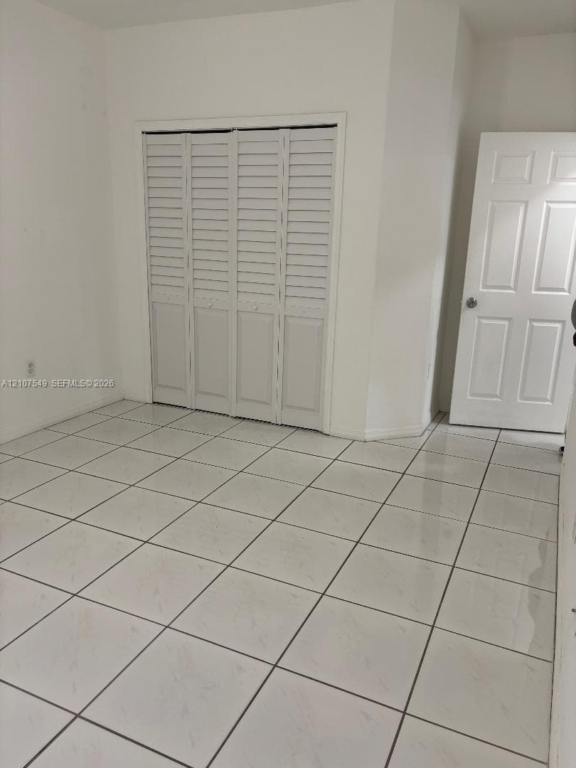 Large-format white tile flooring, four-panel interior door with brushed metal hardware, and bi-fold louvered closet doors