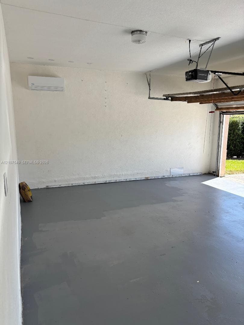 Garage space featuring finished gray flooring, wall-mounted ductless climate control unit, and overhead garage door opener
