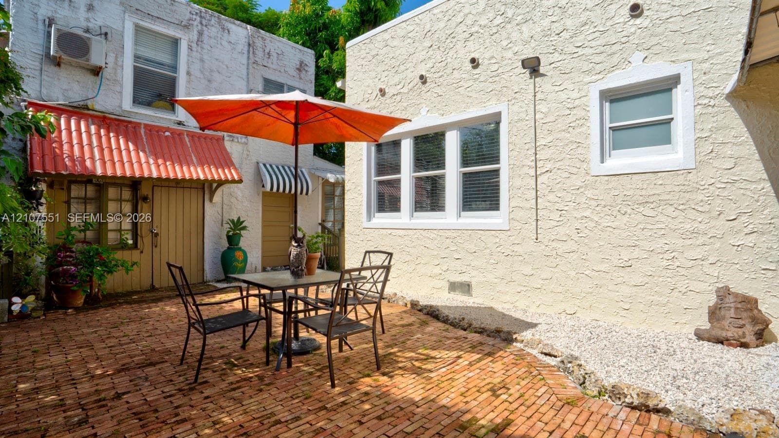Enclosed courtyard featuring a red brick patio, textured stucco exterior walls, multi-pane windows, and a terracotta-style awning