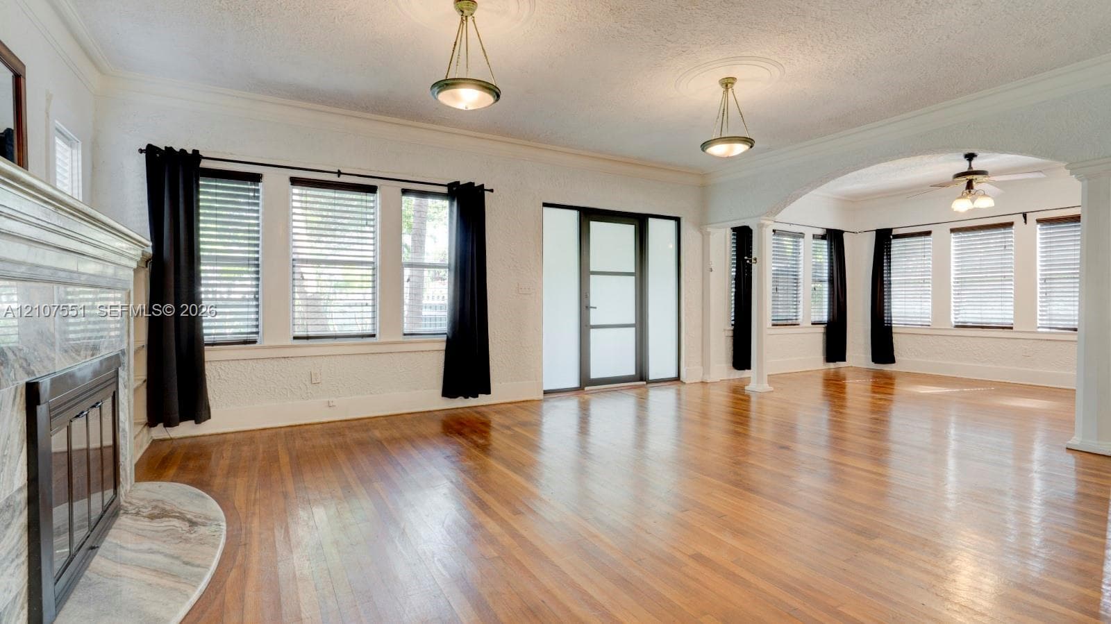 Wood-finish flooring, stone-surround fireplace, arched architectural opening, pendant lighting with decorative ceiling medallions, and multi-pane entry door