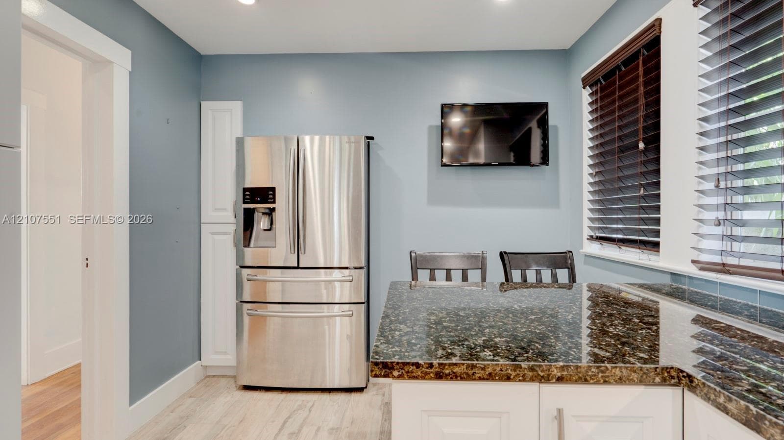 Kitchen featuring stone countertops, white shaker-style cabinetry, stainless steel French-door refrigerator, wood-finish flooring, and horizontal window blinds
