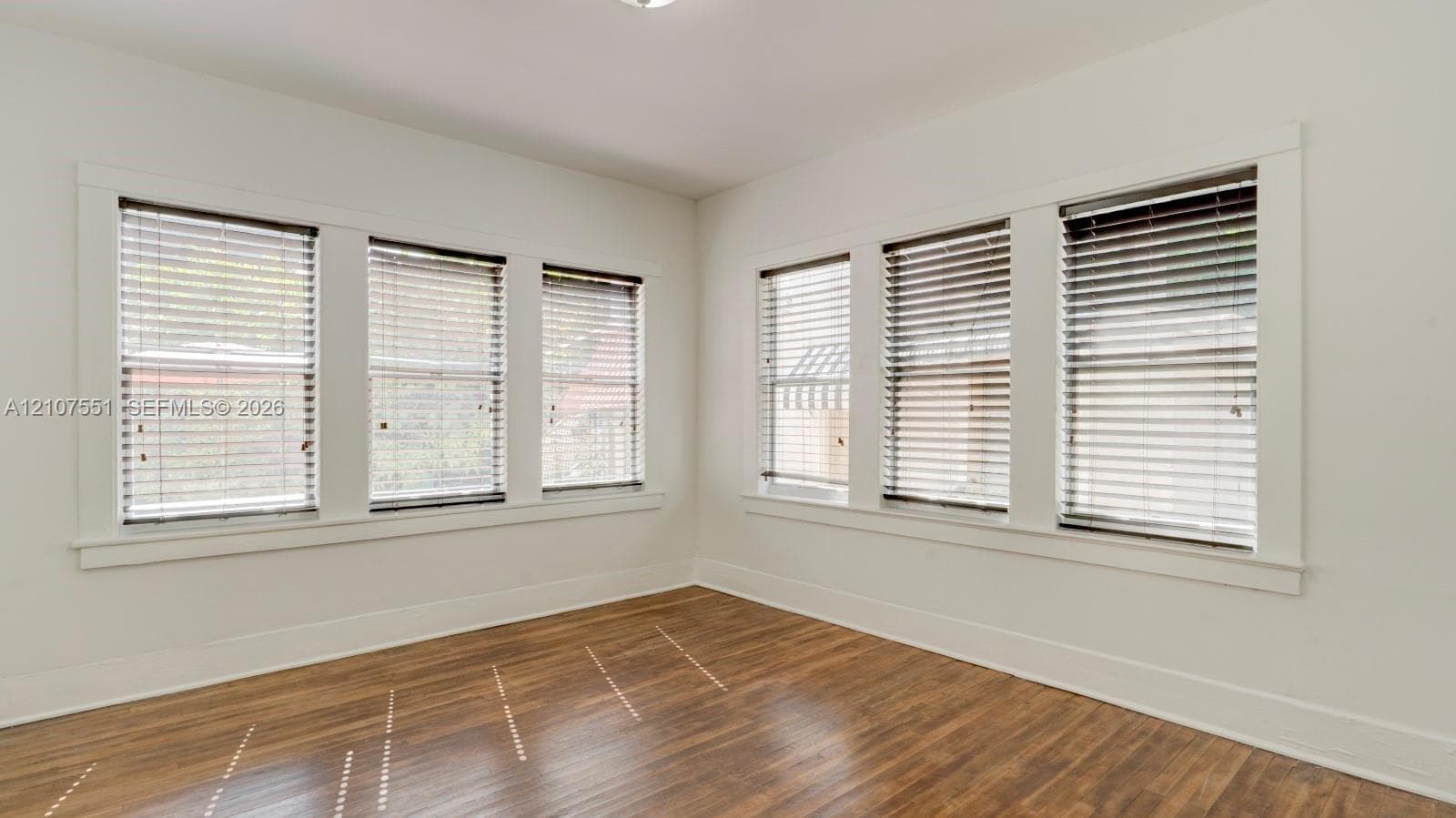 Interior space featuring wood-finish flooring, six windows with horizontal blinds, and clean-lined white trim