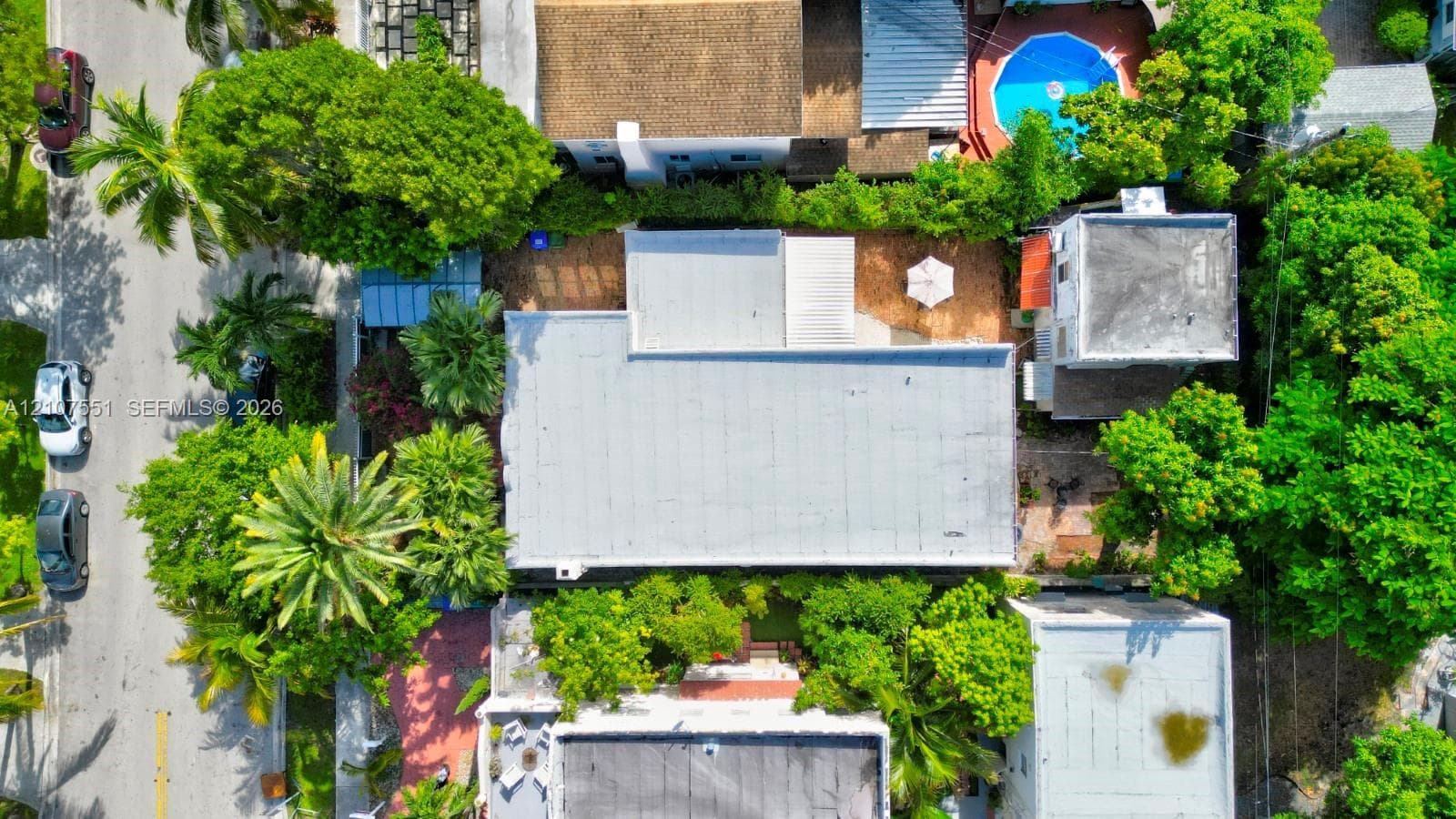 Aerial perspective featuring a flat roofline, mature canopy trees, and paved hardscaping