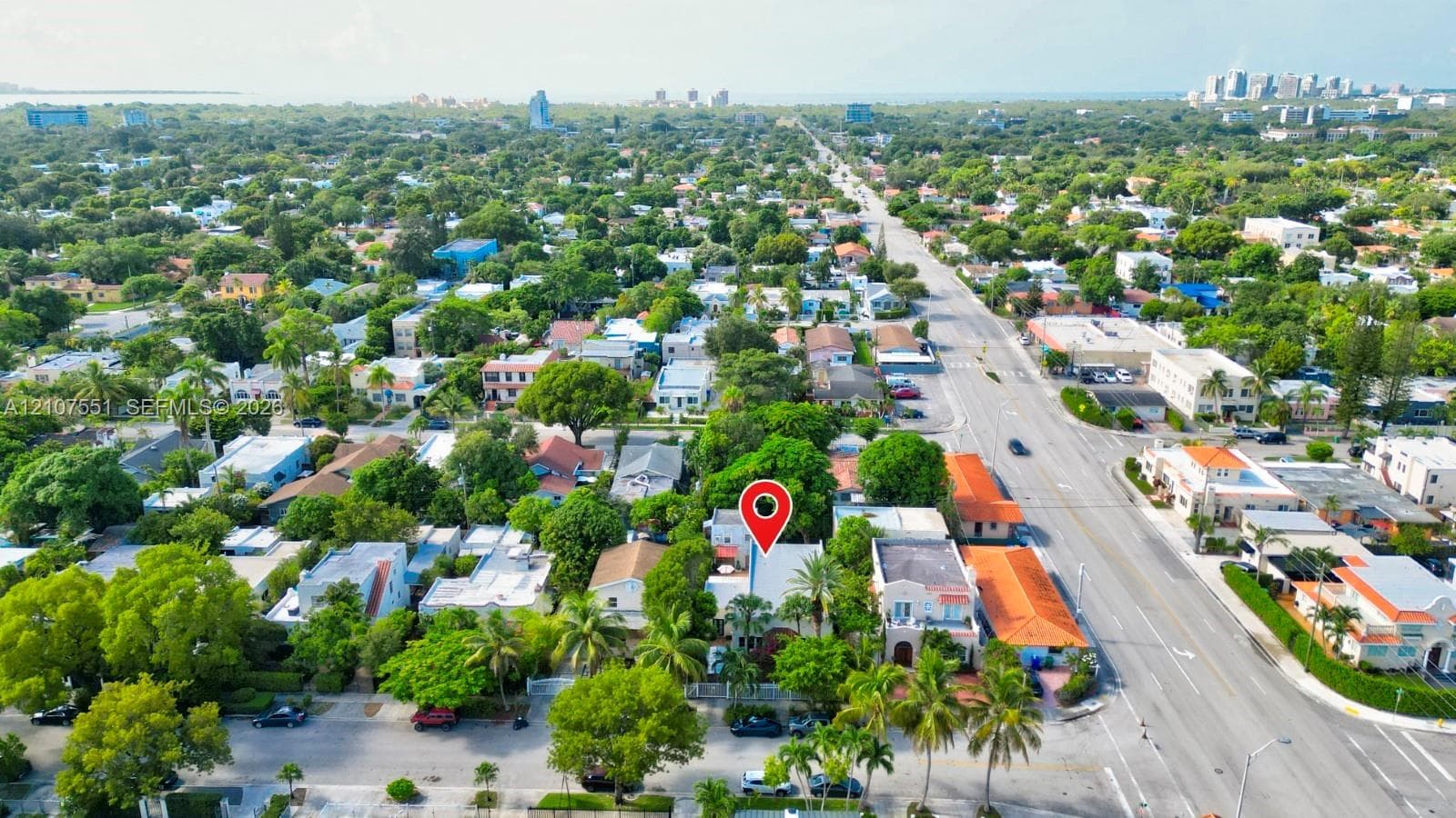 Aerial perspective of a residential property featuring a tree-lined lot, mature palm trees, and proximity to urban infrastructure and coastal city centers