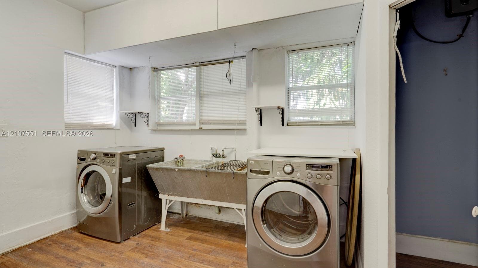 Laundry area featuring wood-finish flooring, a freestanding stainless steel utility sink, and wall-mounted shelving