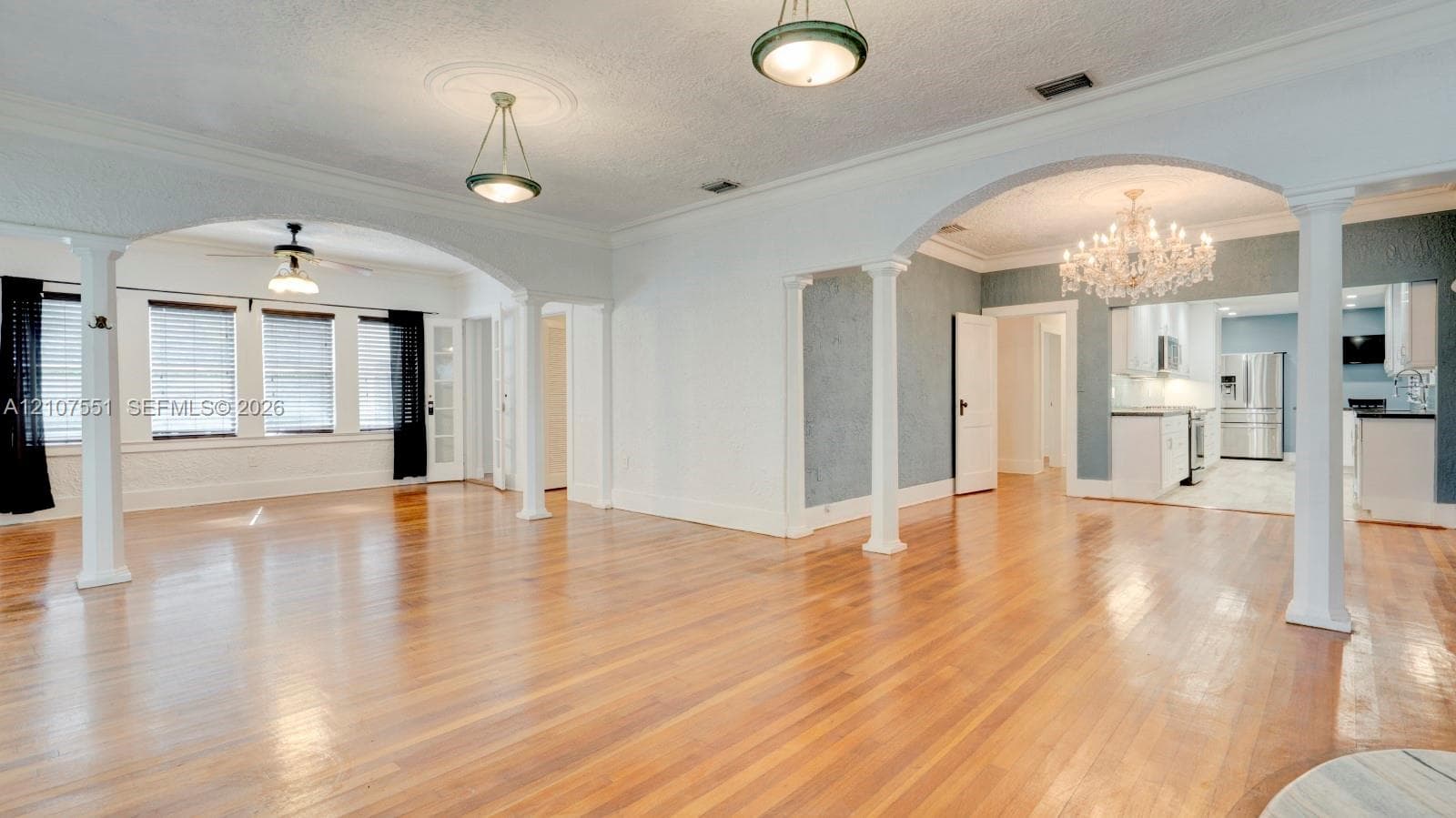Open-concept living space featuring wood-finish flooring, decorative architectural columns, arched entryways, and crystal-style chandelier lighting