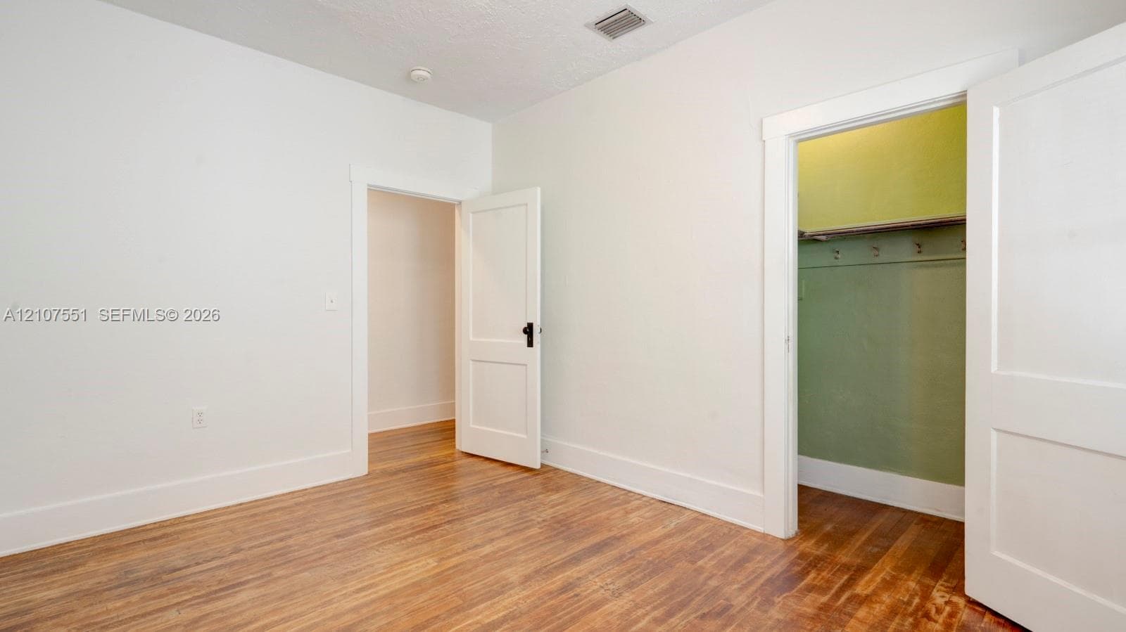 Neutral-toned interior space featuring wood-finish flooring, two-panel interior doors with matte black hardware, and an open storage area with integrated shelving