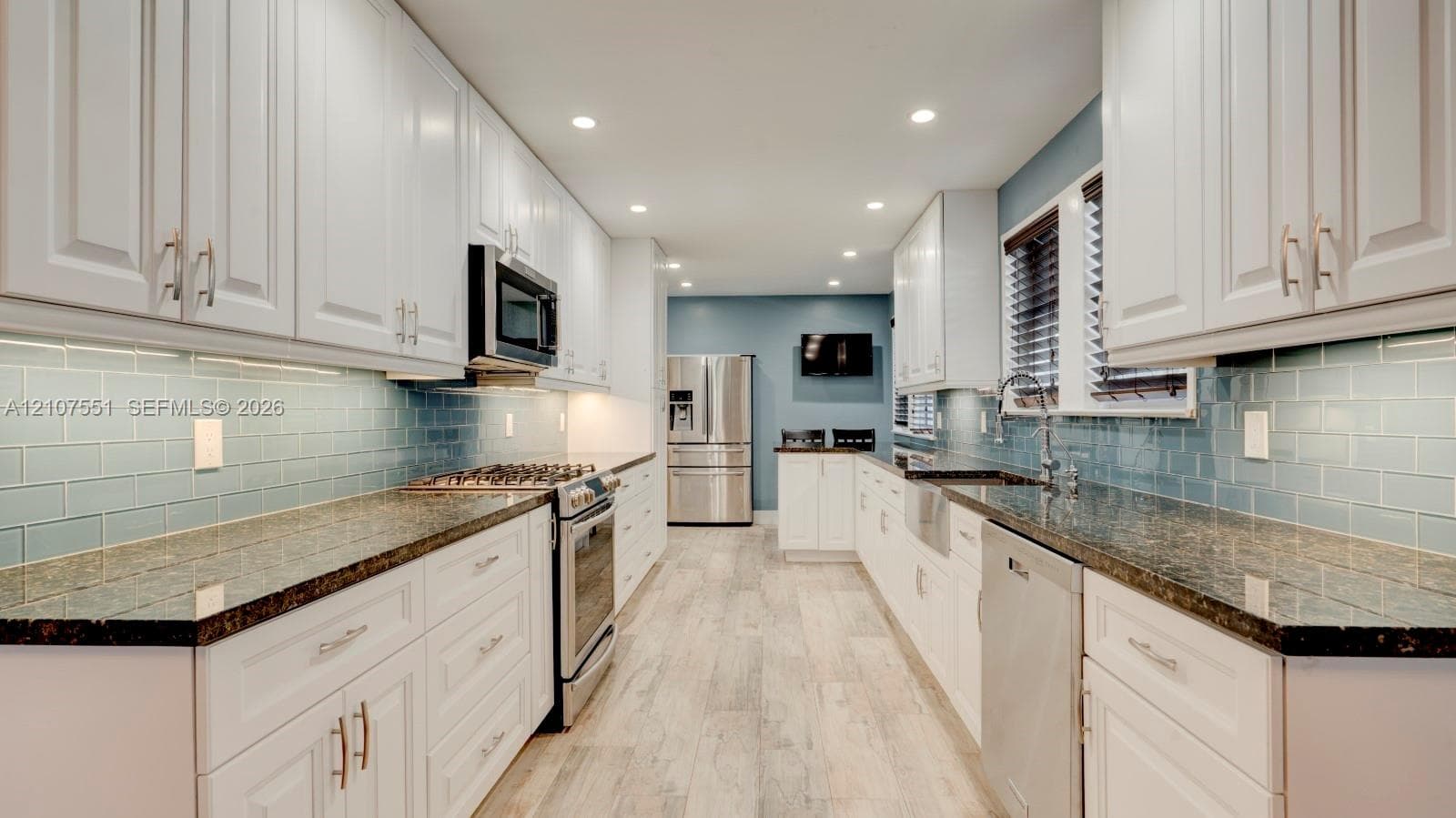 Kitchen featuring shaker-style white cabinetry, dark stone countertops, blue subway tile backsplash, stainless steel appliances, and wood-finish flooring