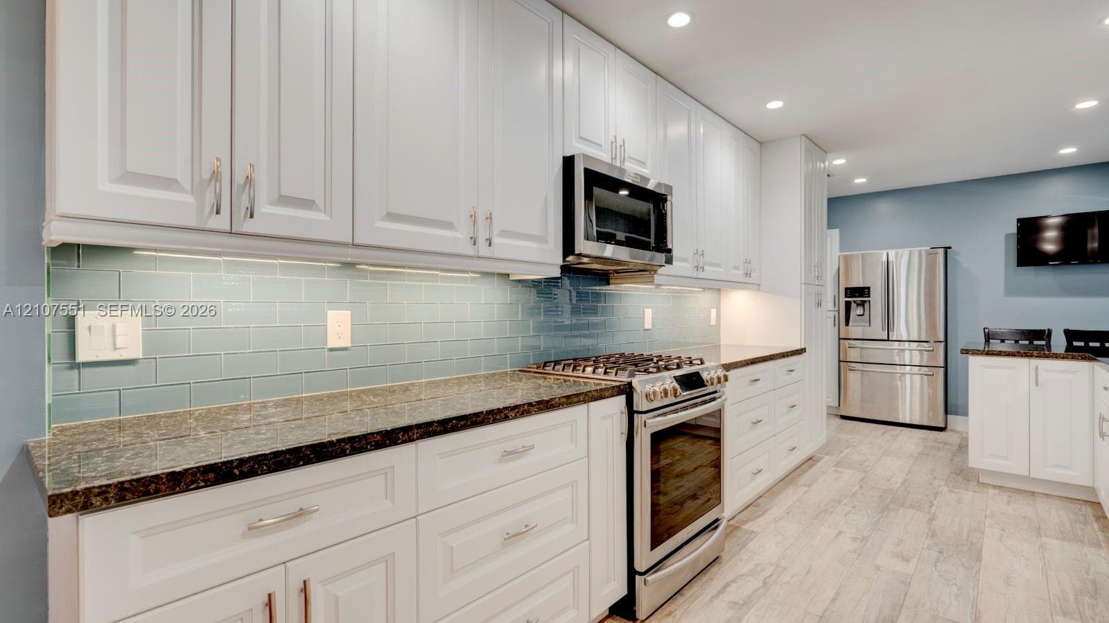 Kitchen featuring white shaker-style cabinetry, stone countertops, a blue glass subway tile backsplash, stainless steel appliances, and wood-finish flooring