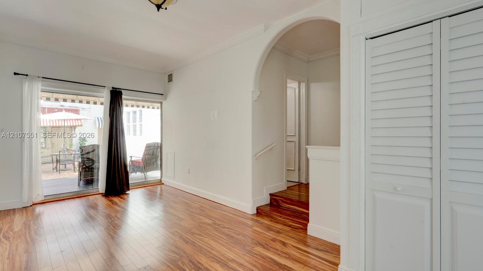 Interior space featuring wood-finish flooring, a decorative architectural archway, floor-to-ceiling sliding glass doors, louvered closet doors, and hardwood-surfaced stairs