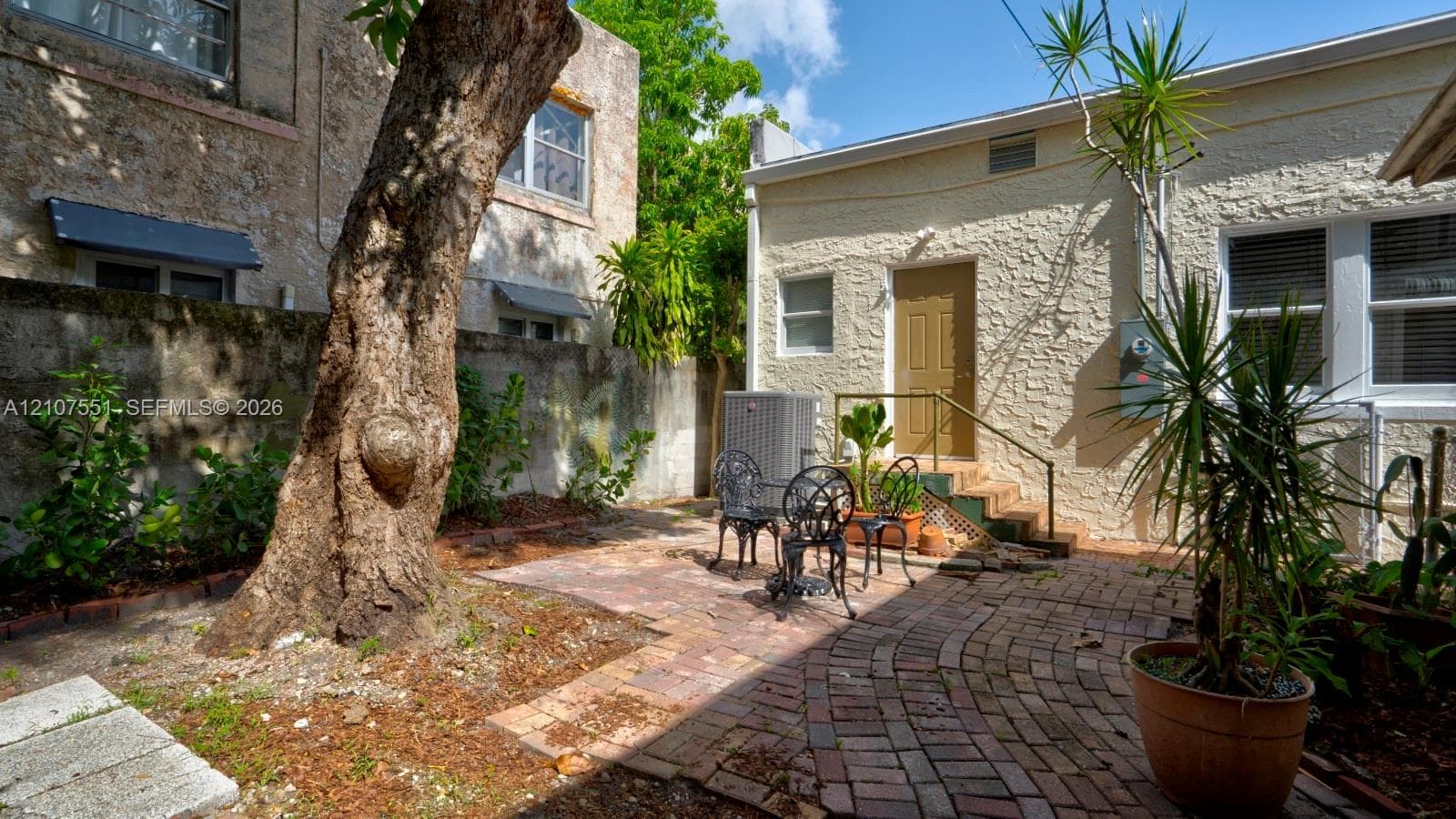Private outdoor courtyard featuring decorative brick pavers, stucco exterior wall finishes, and a mature shade tree