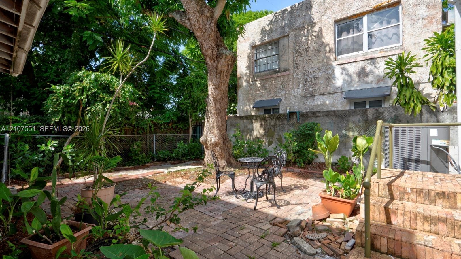 Exterior courtyard featuring brick paving, mature trees, and masonry wall boundary