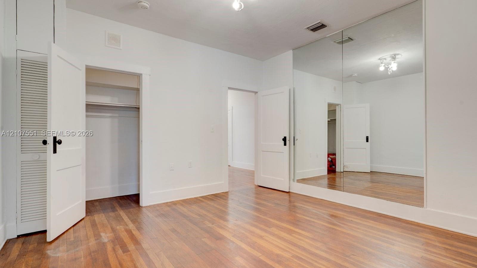 Interior space featuring wood-finish flooring, a wall-to-wall floor-to-ceiling mirror, and solid-core panel doors with matte black hardware