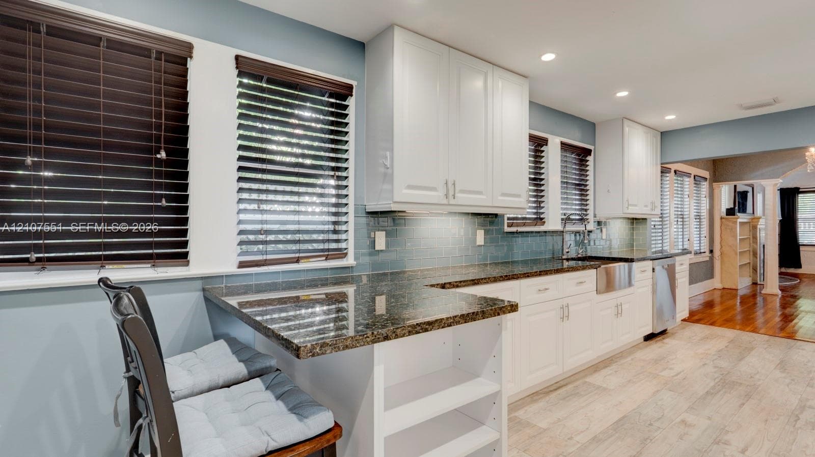 Kitchen featuring white shaker cabinetry, stone countertops, farmhouse-style sink, subway tile backsplash, and wood-finish flooring