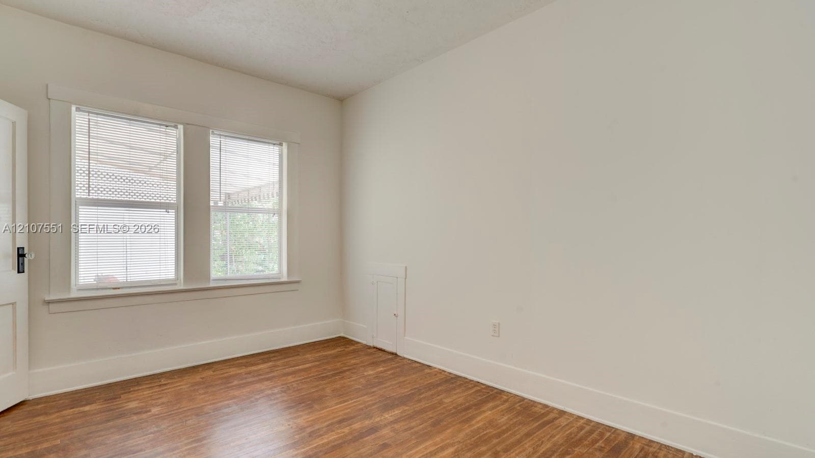 Interior room featuring wood-finish flooring, dual windows with decorative millwork casing, and a built-in wall access panel
