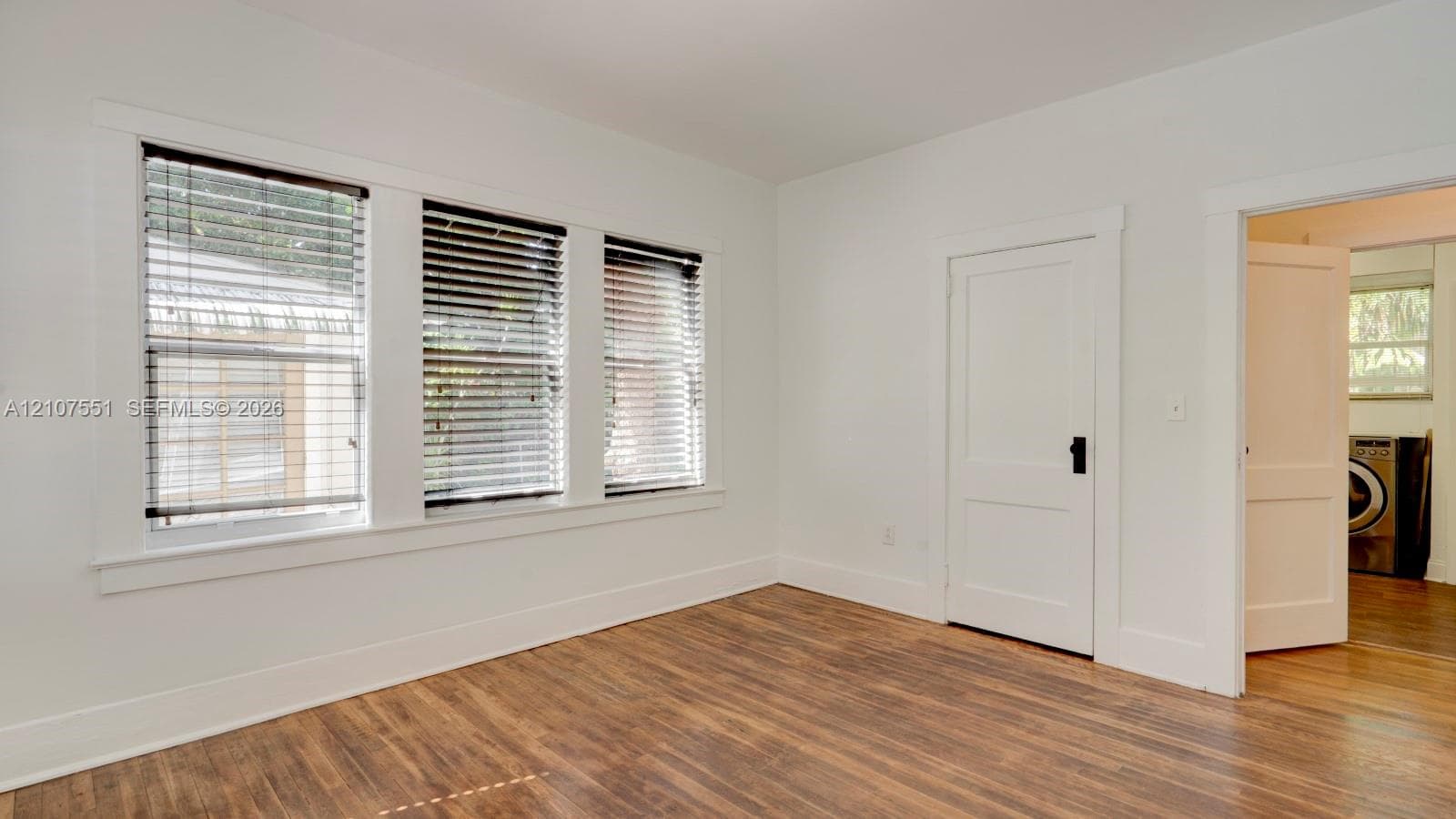 Neutral interior featuring wood-finish flooring, white walls, and triple-pane window configuration with classic millwork trim