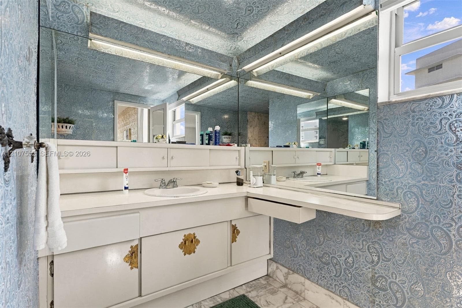 Built-in white vanity with integrated cabinetry, polished gold-toned hardware, solid-surface countertop, circular drop-in sink, and expansive wall-to-wall mirror
