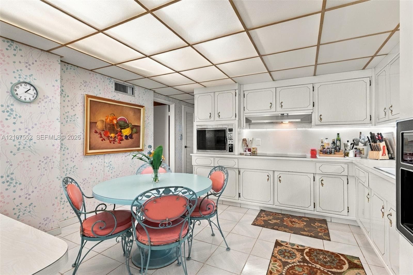 Kitchen featuring white cabinetry, integrated stainless steel appliances, ceramic tile flooring, and a grid-style drop ceiling