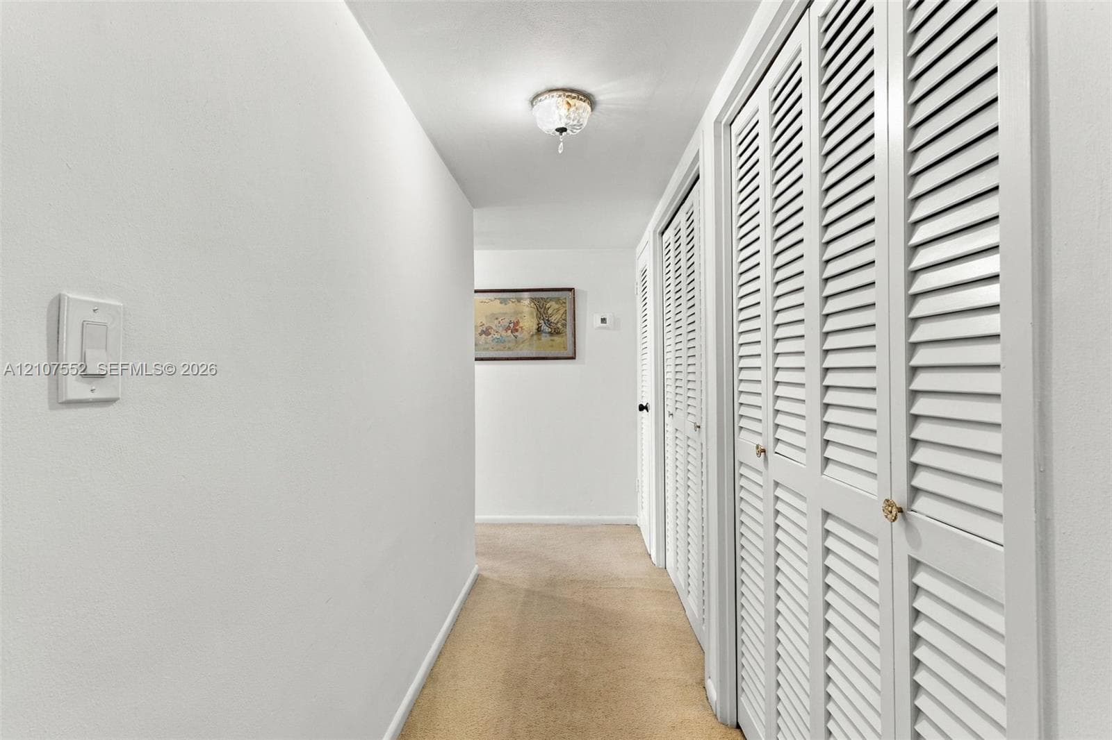 Hallway to 3 huge bedrooms featuring white walls, carpeted flooring, and multiple sets of white louvered-style closet doors