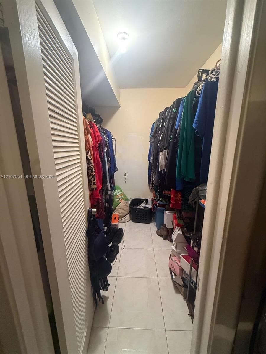 Walk-in closet featuring floor-to-ceiling tile flooring, built-in dual-tier storage rods, and louvered entry door