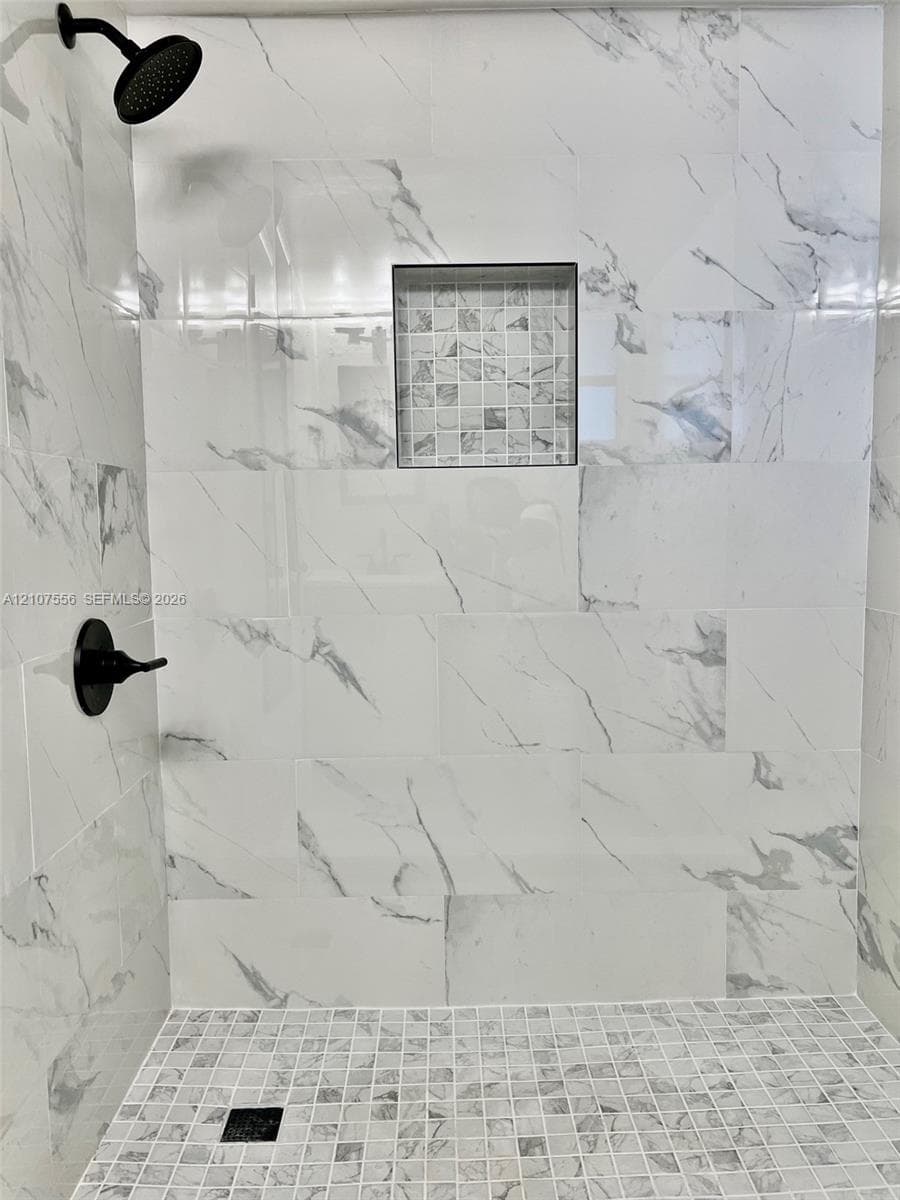 Walk-in shower featuring large-format patterned wall tile, mosaic tile flooring, a recessed storage niche, and matte black plumbing fixtures