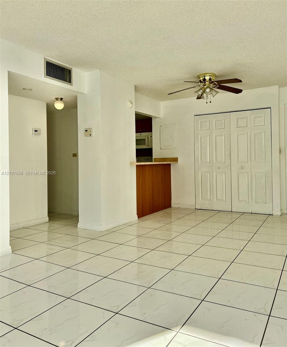 Large-format tile flooring, built-in wooden breakfast bar, ceiling fan with integrated lighting, and dual-panel closet doors
