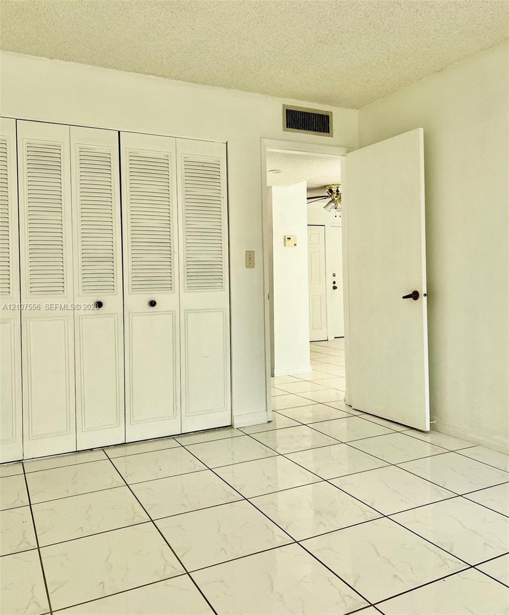 Room featuring gloss-finish tiled flooring and floor-to-ceiling closets with louvered doors