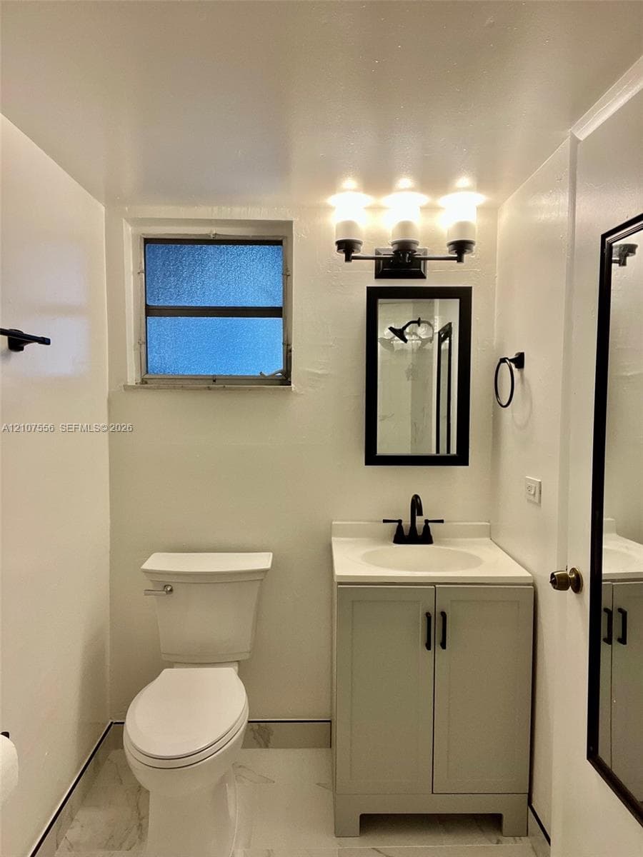 Bathroom featuring a vanity with a white countertop and dark hardware, three-light wall fixture, framed mirror, and tiled flooring