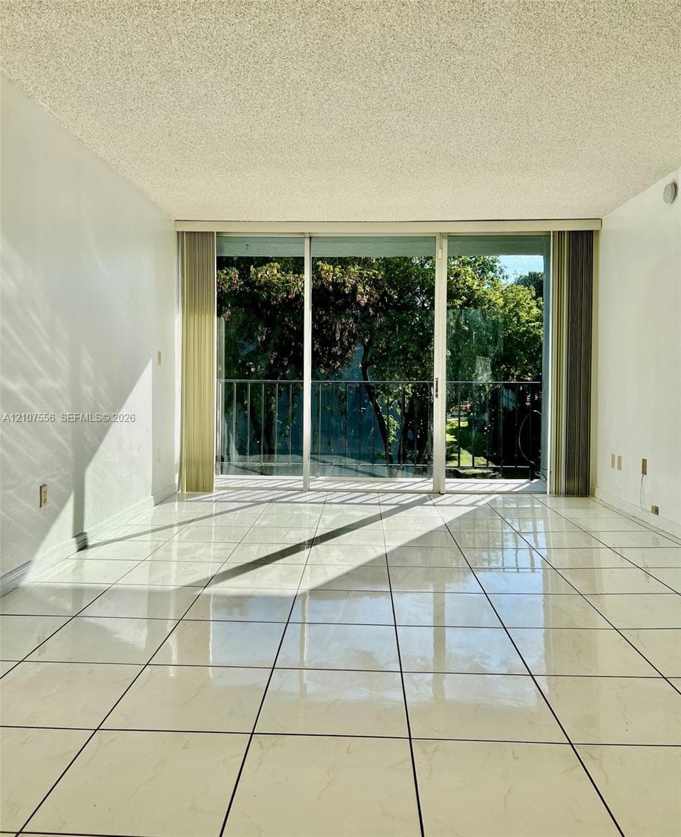 Large-format tile flooring, expansive sliding glass doors, and a private metal-railing balcony featuring mature tree foliage