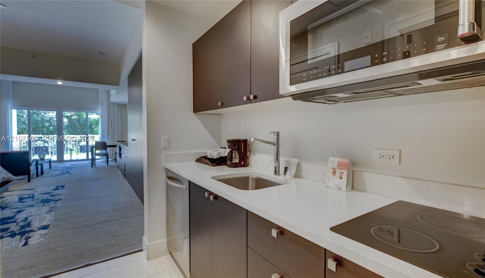Kitchenette featuring dark-finish cabinetry, solid-surface countertops, a stainless steel undermount sink with a gooseneck faucet, an integrated cooktop, and a stainless steel over-the-range microwave