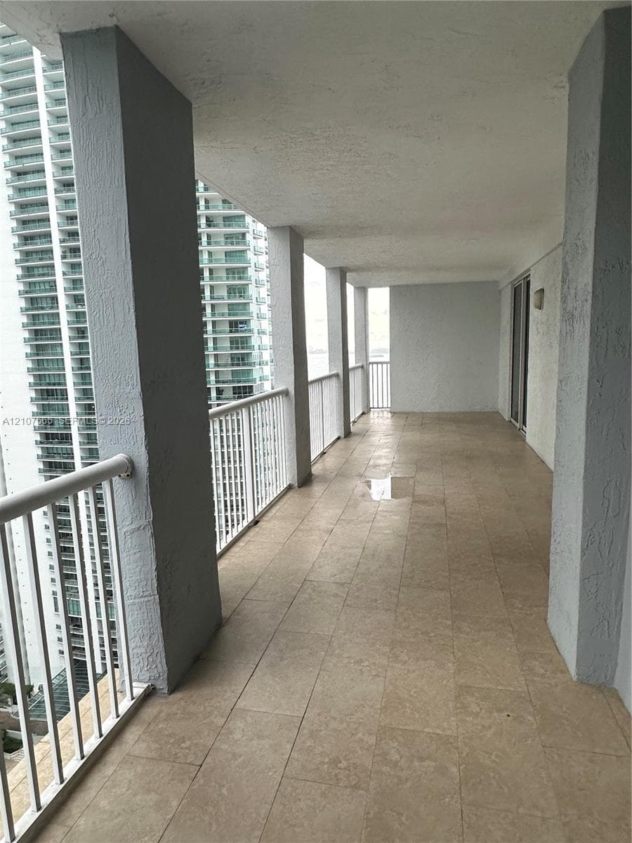 Covered balcony featuring stone-finish tile flooring, textured structural columns, and white metal railings