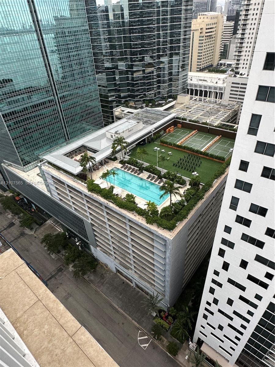 Rooftop amenity deck featuring a rectangular swimming pool, tennis courts, synthetic turf lawn area, and perimeter landscaping