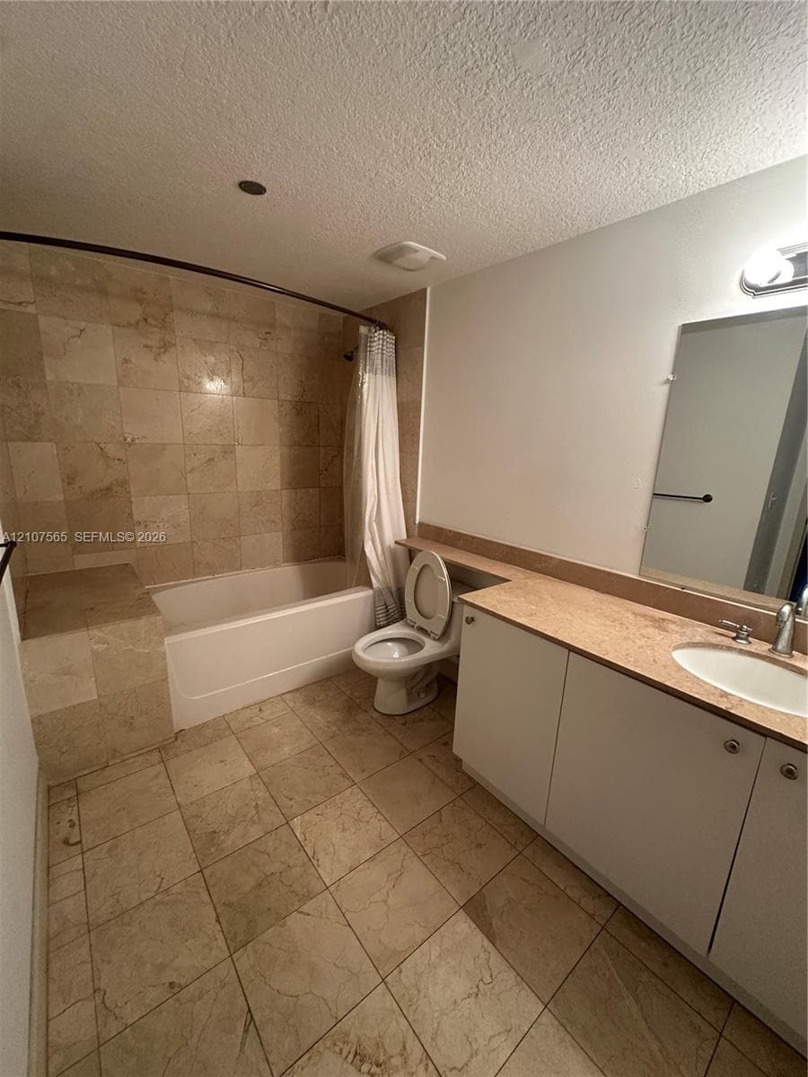 Bathroom featuring natural stone tile flooring, a tub-shower combination with floor-to-ceiling stone tile surround, a built-in tiled tub bench, and a vanity with a stone countertop
