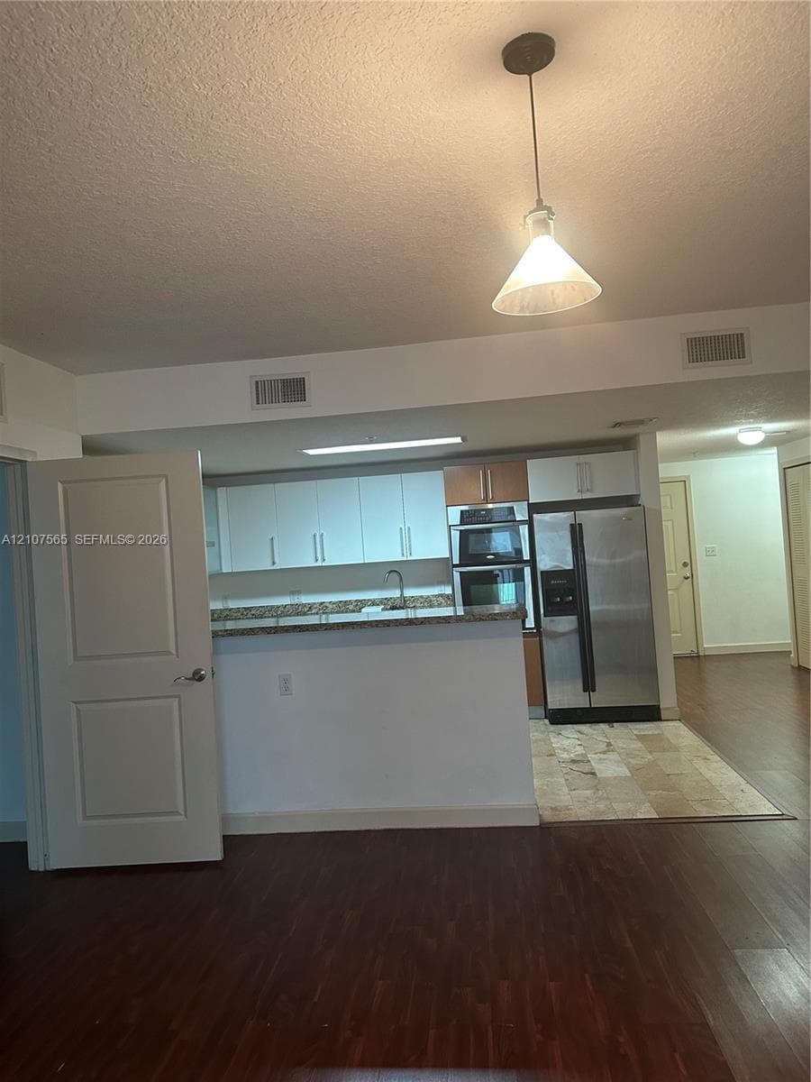 Kitchen featuring white cabinetry, stone-finish countertops, built-in double wall ovens, stainless steel refrigerator, and pendant lighting