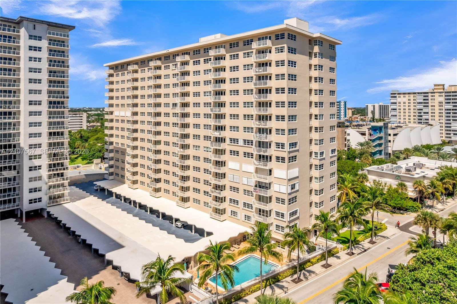 High-rise residential exterior featuring private balconies, ground-level pool, and covered parking structure