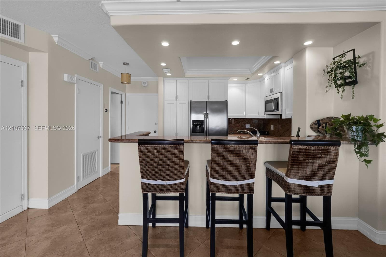 Kitchen featuring white shaker-style cabinetry, stone countertops, stainless steel appliances, breakfast bar, and recessed lighting