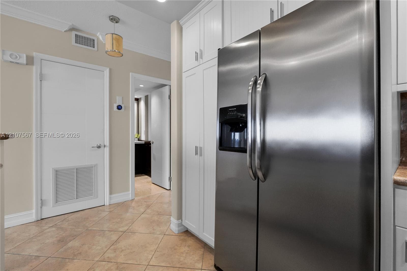 Stainless steel side-by-side refrigerator, full-height white built-in cabinetry, and ceramic tile flooring