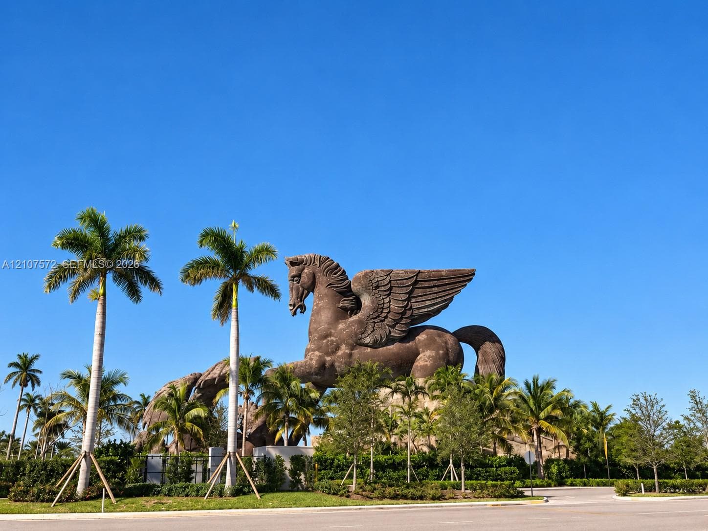 Large-scale winged horse sculpture featuring detailed stone-textured masonry, set within a landscaped perimeter of mature palm trees and manicured vegetation