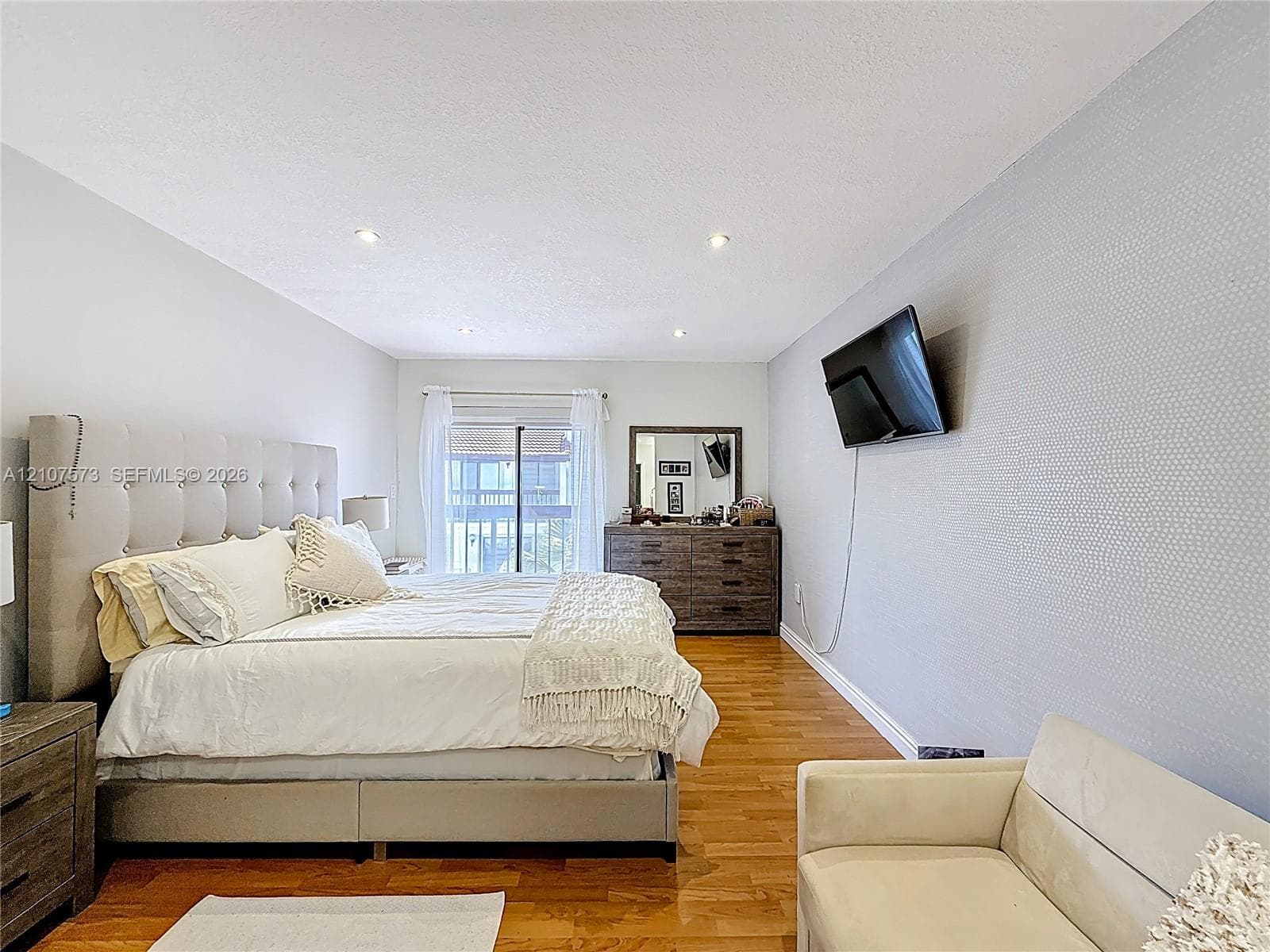 Interior space featuring wood-finish flooring, recessed lighting, and a textured accent wall with sliding glass door access to an exterior balcony