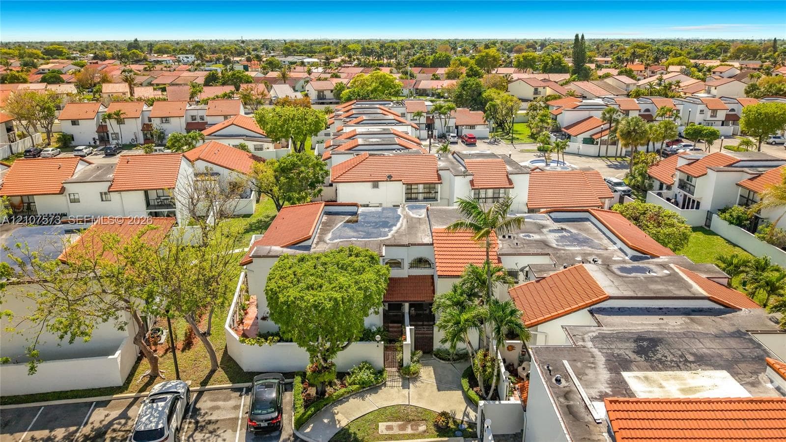 Aerial perspective featuring Spanish-style tile roofing, stucco exterior finishes, mature palm trees, and designated surface parking