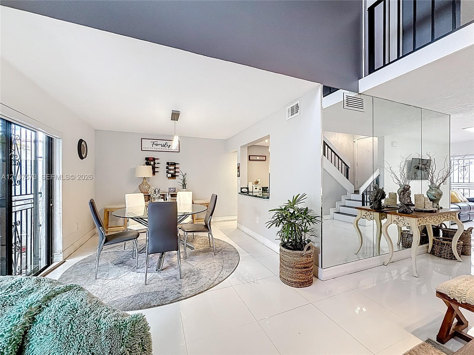 Open-concept interior featuring large-format tile flooring, double-height ceilings, mirrored wall accents, and an integrated staircase with a black metal railing