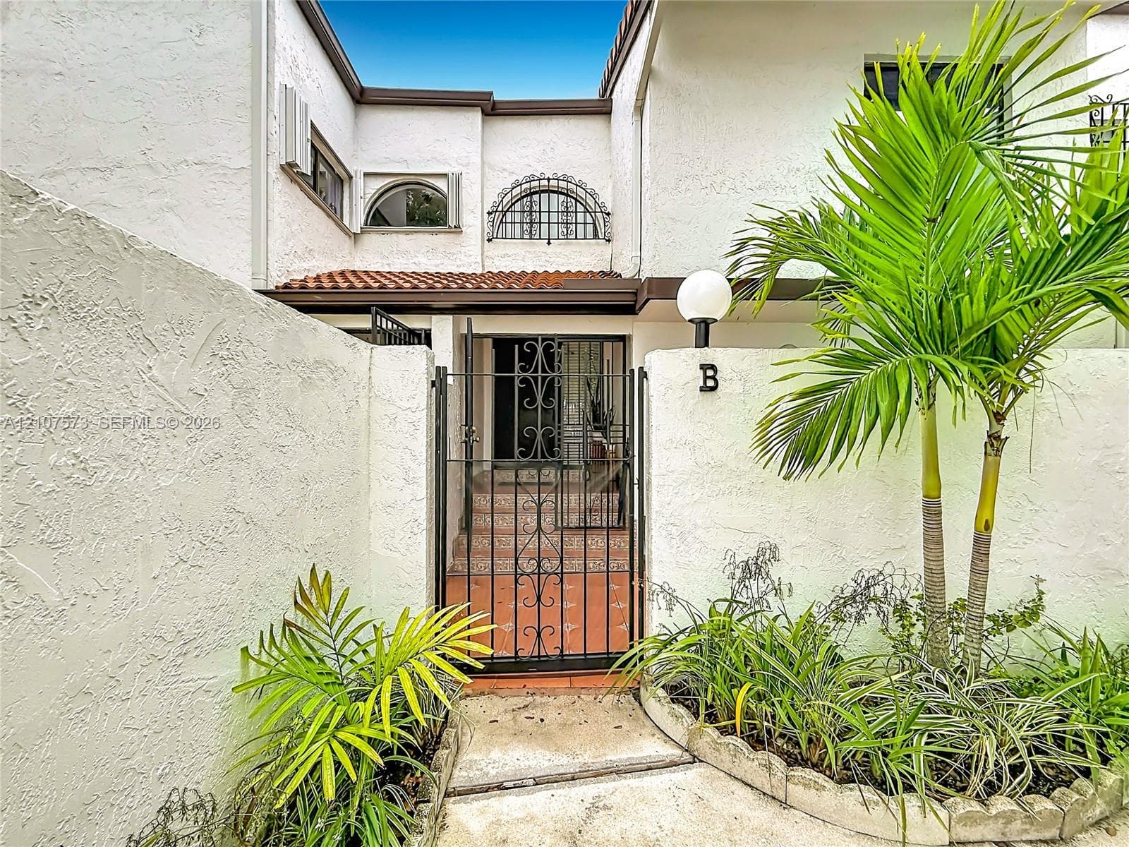 Stucco exterior featuring arched windows with decorative metal grilles, a gated courtyard entry, terracotta-style paving, and attached globe lighting