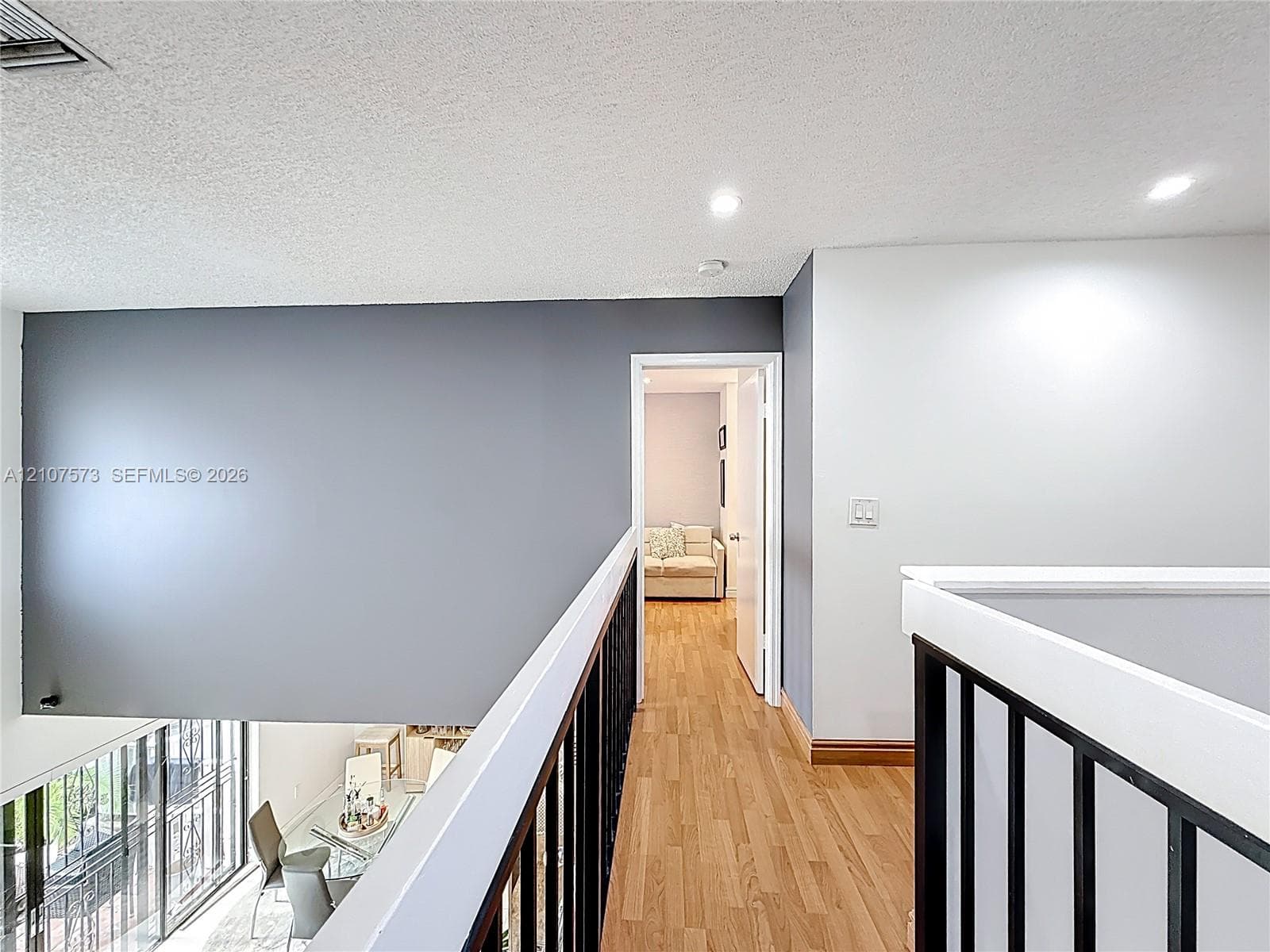 Hallway featuring wood-finish flooring, metal vertical-bar railing, and recessed ceiling lighting