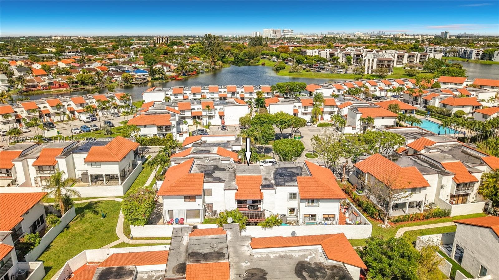Aerial perspective of a multi-unit residential community featuring red tile roofs, stucco exterior finishes, and proximity to community water features and a swimming pool