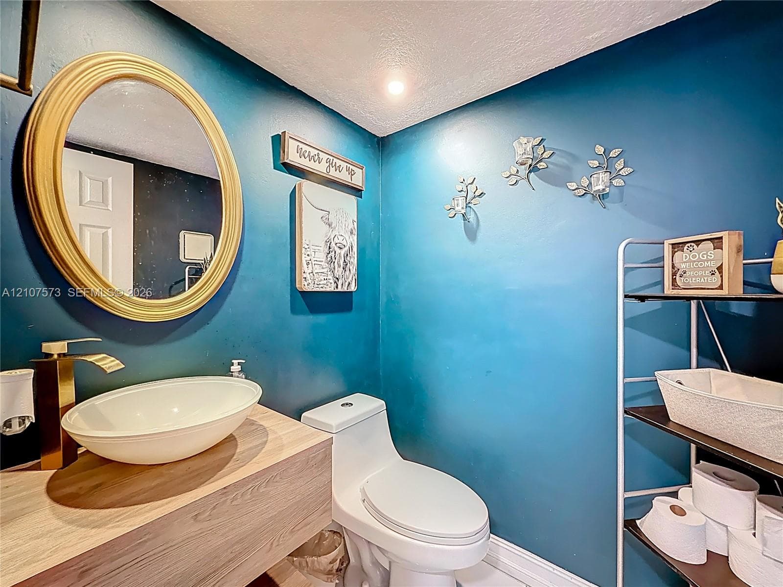 Floating wood-finish vanity with an oval vessel sink and metallic finish faucet, accompanied by an oval-framed wall mirror and wall-mounted light fixtures