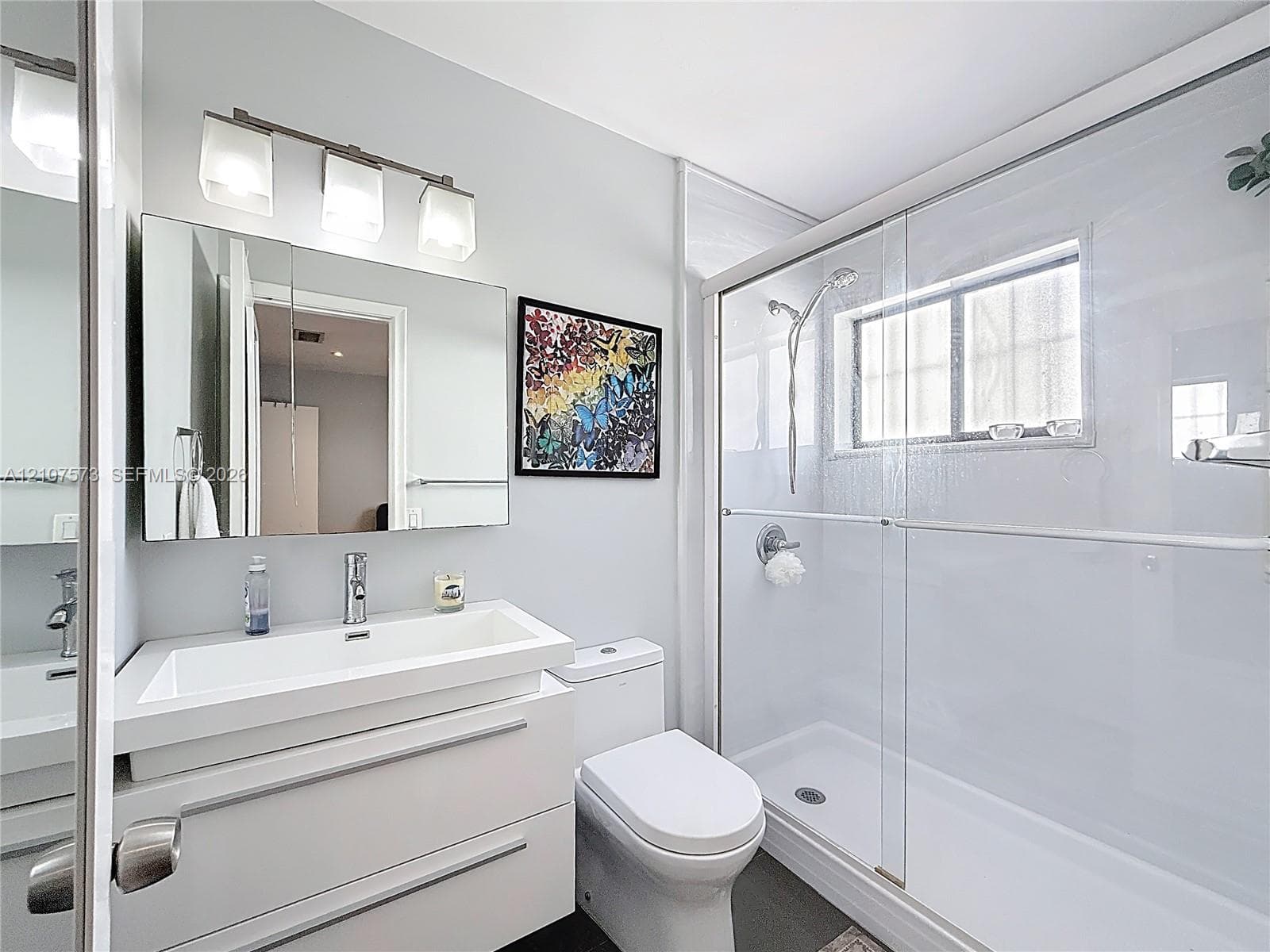 Modern floating vanity with a rectangular sink, three-light wall fixture, glass-enclosed shower with a handheld showerhead, and a medicine cabinet mirror