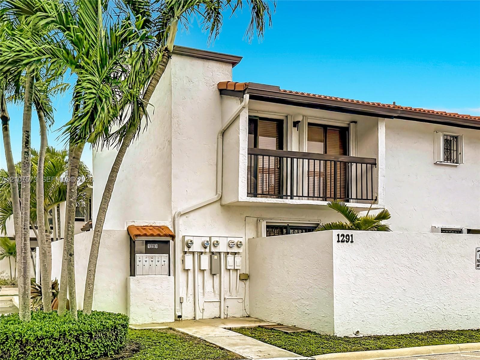 Two-story exterior featuring white stucco finish, tile roof accents, metal balcony railing, and concrete perimeter wall